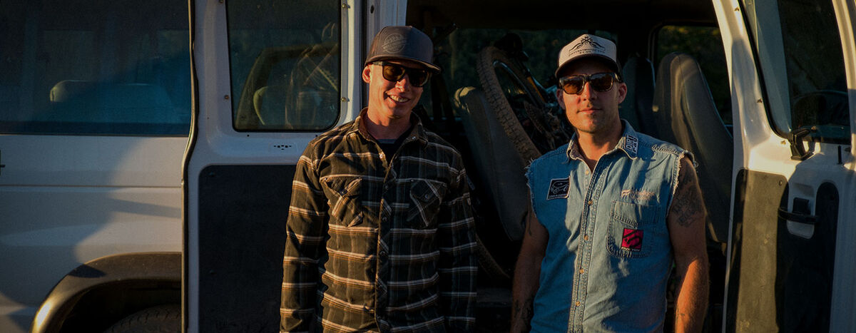 Two men in ball caps standing in front of an open van.