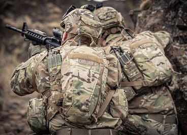 Two soldiers kneeling with camo hydration packs on.